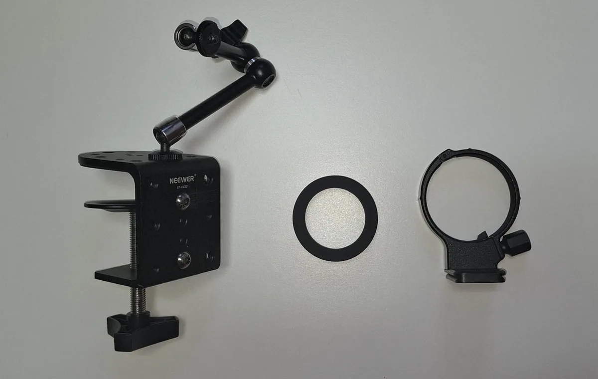 The three parts of the DIY Handy mount laid out on a neutral background: a NEEWER C-clamp with articulated arm, a silicone spacer ring, and a Sigma tripod ring