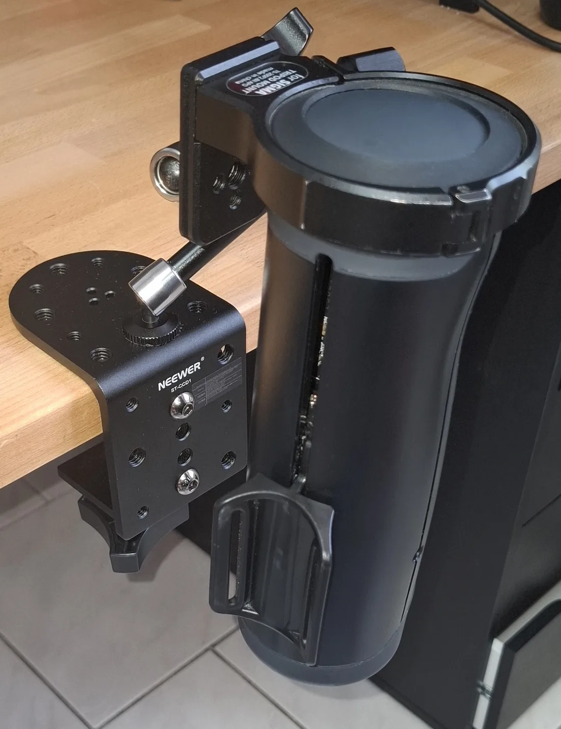 A Handy held hands-free at the edge of a desk by a NEEWER photography C-clamp and a Sigma tripod ring, with no sleeve fitted so the mount is fully visible